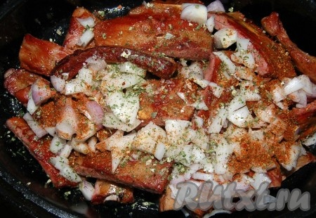 Обжаренные копченые ребрышки переложить в жаровнюи добавить нарезанный репчатый лук. Добавить соль, перец, специи и подлить горячую воду.