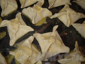 Сформированные конвертики с начинкой выложите на противень, предварительно застеленный пергаментом. Отдельно взбейте сырое яйцо вилкой до получения однородной массы. Смажьте взбитым яйцом каждый конвертик.