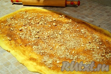 Для начинки растереть масло комнатной температуры с корицей, сахаром, отставить в сторону. Как только тесто подошло, раскатать его на присыпанной мукой поверхности как можно тоньше в прямоугольник, распределить начинку и орехи, оставляя по 1 см со всех сторон, закатать тесто в рулет.
