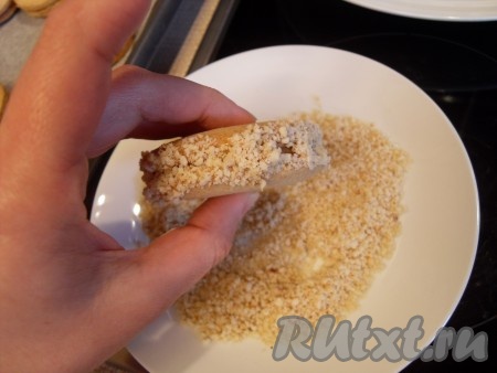 Слегка нанести сгущенку на бока и прокатать печенье, как колесико, по орехам.