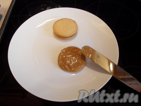 Сборка печенья "Альфахорес". Орехи высыпать в тарелку. Одну половинку печенья смазать сгущенкой, приклеить вторую половинку.
