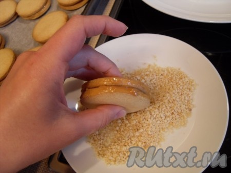 Слегка нанести сгущенку на бока и прокатать печенье, как колесико, по орехам.