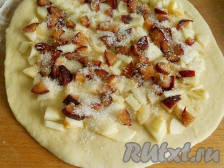 Поднявшееся тесто обмять, на присыпанной мукой поверхности раскатать в лепёшку толщиной около 0,5 сантиметра. Растопить сливочное масло, смазать им поверхность раскатанного теста. Яблоки очистить от кожуры, удаляя семенную коробочку, нарезать на небольшие кусочки. Я ещё добавила немного слив, но это по желанию. Разложить яблоки и сливы по поверхности теста. Сверху присыпать начинку 2 столовыми ложками сахара.