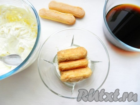 Ликер добавить в кофе. В форму для десерта выложить немного крема. Печенье савоярди обмакнуть в кофе с ликером и выложить на крем.