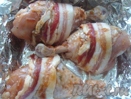 Обернуть каждую куриную ножку беконом, при необходимости закрепить шпажкой. Запекать в разогретой до 180 градусов духовке 25-30 минут, перевернуть 2-3 раза.
