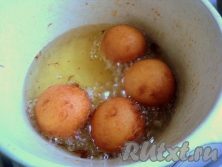 В кастрюле (или в сковороде с высоким бортиком) нагреть достаточное количество растительного масла. При помощи столовой ложки выкладывать тесто в кипящее масло в виде клецок и жарить на среднем огне до румяности со всех сторон. Чтобы пончики быстро не зажаривались сверху и успевали пропечься изнутри, огонь должен быть ниже среднего. Готовые пончики вначале выкладывать на бумажные салфетки, чтобы убрать лишнее масло, а затем перекладывать на тарелку для подачи. Постепенно пожарить все пончики.