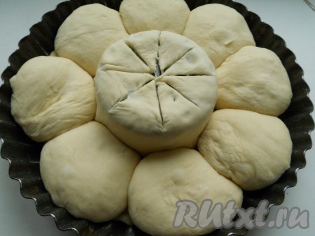 Большую часть теста раскатать в лепешку. На дно круглой формы (д. 22-23 см), посередине поместить вверх дном маленькую полукруглую миску или банку. Выложить тесто в форму, накрывая банку. Остальные 8 частей теста скатать в колобки и разместить по краям формы. Сделать сверху теста разрезы (на 8 частей).