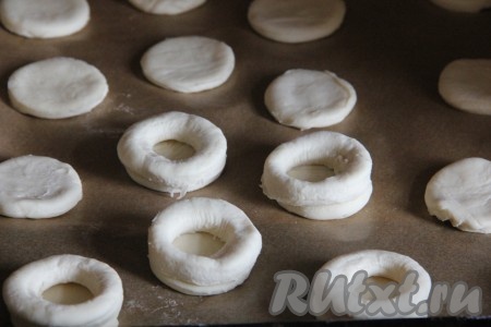 Теперь  приступаем к формированию волованов. Удобнее всего формировать их сразу на противне, застеленном пергаментом (если не уверены в качестве бумаги для выпечки, то предварительно смажьте её немного растительным маслом). На застеленный противень на некотором расстоянии друг от друга выкладывать кружочки, вырезанные из слоёного теста. "Бублики" из теста смочить с одной стороны водой и влажной стороной выложить на круги из теста. Получатся заготовки волованов, состоящие из двух частей теста, напоминающие "колодец" или "башенку". Из остатков теста точно также сформировать ещё волованы, раскатав тесто, вырезав и сформировав из него заготовки. 