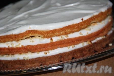 Арахис обжарить на сухой сковороде и измельчить в блендере. Собрать бисквитный торт: выложить шоколадный корж, смазать его белковым кремом и посыпать дроблёными орехами. Затем положить красный корж, смазать его кремом и посыпать орехами. Затем положить ванильный корж и тоже смазать кремом (орехами верх не покрываем).