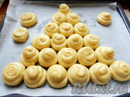 В небольшой ёмкости соединить яичный желток и молоко, перемешать, смазать булочки этой смесью при помощи кулинарной кисти. Сверху немного присыпать коричневым (или обычным) сахаром. Оставить противень с булочками в тёплом месте для подхода выпечки на 20 минут.