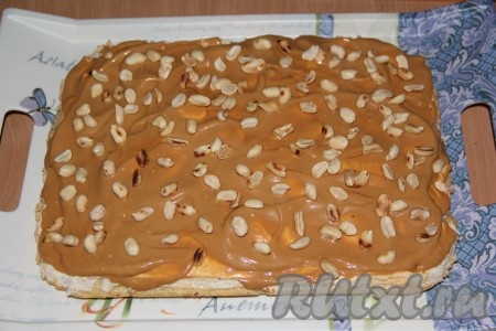 Собрать торт "Сникерс": выложить корж на поднос, сверху выложить половину крема, аккуратно разровнять. Сверху посыпать орехами.
