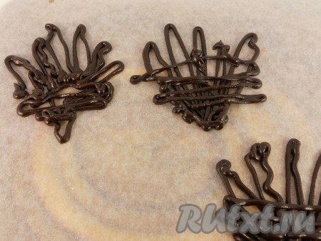 Поместить торт "Сникерс" в холодильник до полного застывания шоколада. Украсить по своему желанию. Предлагаю свой вариант украшения: я оставила 2 ложки шоколадной массы и нарисовала на пергаменте с помощью кондитерского шприца шоколадные короны (поместить в холодильник, пока не застынет шоколад, затем аккуратно отделить коронки от бумаги).