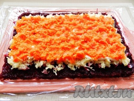 Затем разложить слой натёртой на мелкой тёрке очищенной моркови, также отступая по 1 сантиметру от длинной стороны слоя картофеля.