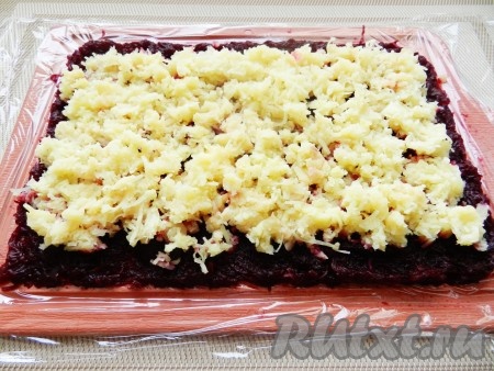 На слой свеклы равномерно разложить слой очищенного и натёртого на мелкой тёрке картофеля, подсолить немного. Слой картофеля должен быть меньше свекольного примерно на 1 сантиметр с двух длинных сторон. На картофель нанести сетку из майонеза.