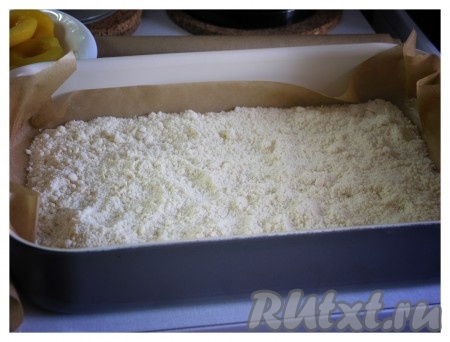 Глубокий противень (или форму для выпечки) застелить бумагой для выпечки. Половину получившейся крошки рассыпать рукой по противню.