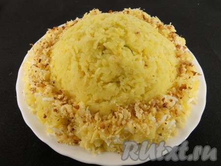 Половиной оставшегося натертого картофеля покрыть салат и немного прижать, снизу сформировать бортик, чтобы получился вид шапки. Остальной картофель смешать с натертым на мелкой терке белком и второй половиной тертого сыра. Вокруг салата выложить в виде опушки. Сверху посыпать оставшимися измельченными орехами, имитируя мех.