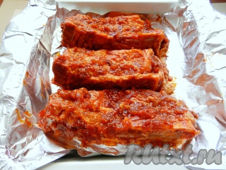 Смазать свиные рёбрышки соусом из мёда, горчицы и кетчупа со всех сторон. Выложить в форму для запекания, застеленную фольгой. Запечь рёбрышки в разогретой духовке при температуре 200 градусов в течение 50 минут.