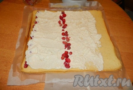 Размазываем начинку, добавляем ягоды и сворачиваем. Делаем все быстро, чтобы свернуть его не остывшим, иначе будет плохо отлепляться от бумаги.
