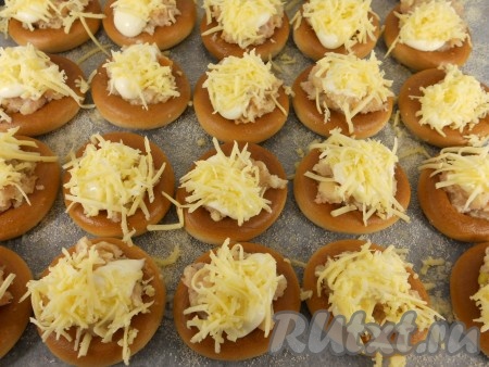 Фарш, выложенный поверх бубликов, смазать майонезом и посыпать натёртым сыром.