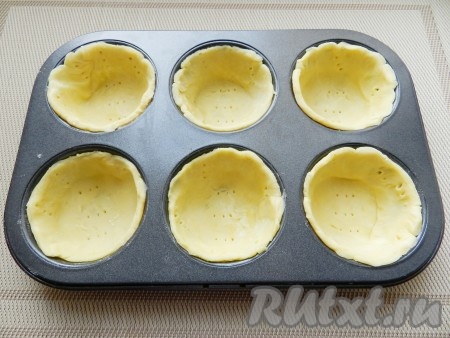 Тесто достать из холодильника, раскатать и вырезать из него 10 кругов диаметром больше, чем форма для выпечки. Форму для выпечки смазать маслом, выложить тесто, разровнять и наколоть вилкой в нескольких местах.