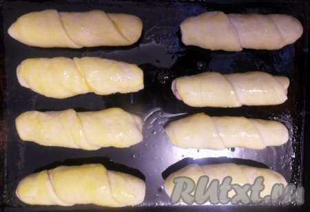 На смазанный растительным маслом противень выложить сосиски в тесте. В желток добавить 1 чайную ложку воды и немного соли. Смазать им сосиски. Получится ещё вкуснее, если на смазанные яйцом сосиски в тесте посыпать кунжут. Выпекать до золотистого цвета при температуре 180 градусов (приблизительно 20-25 минут).
