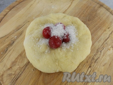 Тесто выложить на стол, присыпанный мукой, обмять немного. Оно получается отличным, "дышащим"! Разделить тесто на кусочки (у меня по 70 грамм - я делала большие пирожки). Руками растянуть кусочки, чтобы получились лепешки. Вишню немного разморозить, выкладывать по 3-5 ягод в центр лепешки. Сверху - по 1 чайной ложке сахара.

