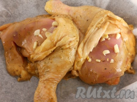 Форму для запекания застелить пергаментной бумагой, выложить маринованные куриные ножки. Под кожу поместить порезанный небольшими кусочками чеснок.
