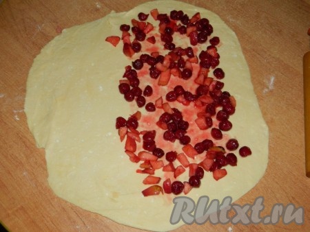 По прошествии 40 минут достать тесто из холодильника. На присыпанной мукой поверхности раскатать тесто в тонкий прямоугольный пласт. Раскатывать тесто лучше до полупрозрачности, тогда штрудель получится очень нежным. На одну половину раскатанного теста, немного отступив от краёв, равномерно выложить начинку из яблок и вишни. 