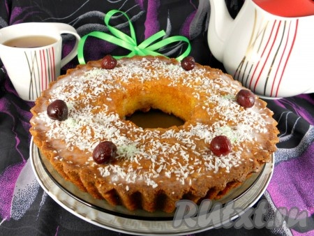 Остывший кекс освободить от жестяной банки, аккуратно повернув ее сначала по часовой стрелке, затем - против. Переложить кекс на блюдо, смазать помадкой и посыпать сверху кокосовой стружкой. Украсить вишнями.