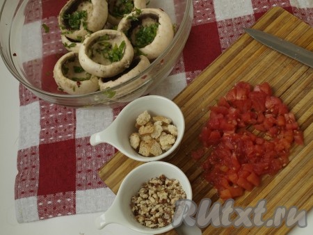 Оливковое масло, пропущенный через пресс чеснок, петрушку, лимонный сок  и мелко порезанный перчик чили смешиваем и полученной смесью натираем шляпки шампиньонов. И пусть шляпки маринуются, пока готовится начинка.

Помидоры кладём в кипяток, чтобы снять с них шкурку. Очищенные от шкурки помидоры режем кубиками. На растительном масле слегка обжариваем порезанный лук и измельченную грибную массу. Орехи рубим достаточно мелко. 