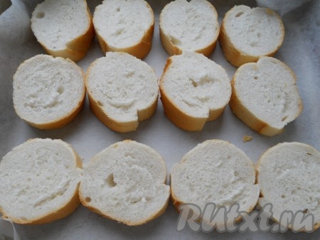 Багет (или батон) нарезать на ломти толщиной около 2-3 сантиметров, выложить на противень, застеленный пергаментной бумагой.