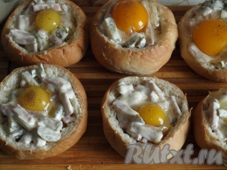 Каждую булочку изнутри смочить половиной столовой ложки молока и смазать&nbsp; сливочным маслом. Добавить начинку из ветчины и огурца, посыпать порезанной зеленью. В каждую булочку вбить по яйцу (если Вы будете готовить с куриными яйцами, то берите не крупные). Желтки посыпать солью и перцем. 
