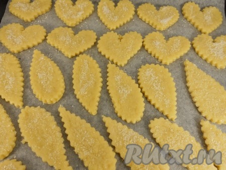 Разделить тесто на 3 части, каждую часть обернуть пищевой плёнкой и поместить в холодильник на 30 минут. Далее каждую часть поочередно доставать из холодильника, на присыпанной мукой поверхности раскатывать в пласт толщиной около 0,5 сантиметров. Вырезать выемками для печенья различные фигурки. Обмакнуть одну сторону печенья в сахар или посыпать сверху. Противень застелить пергаментом и выложить на него печенье.