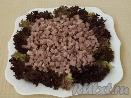 На блюдо, на котором будем подавать салат, выкладываем листья салата. Ветчину режем кубиками, кладём поверх листьев салата, делаем сеточку из майонеза.
