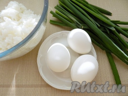 Пока тесто "отдыхает", нужно подготовить начинку. Для этого рис нужно промыть водой, выложить в кастрюлю с кипящей подсоленной водой, перемешать, после закипания воды уменьшить огонь и отварить до готовности (обычно на варку риса требуется минут 20, рисинки должны стать мягкими). Отваренный рис откинуть на дуршлаг, оставить остывать. 3 яйца отварить в течение 10 минут с момента закипания воды, после этого остудить их и очистить. Зелёный лук промыть водой, очищая луковицы, дать немного обсохнуть.