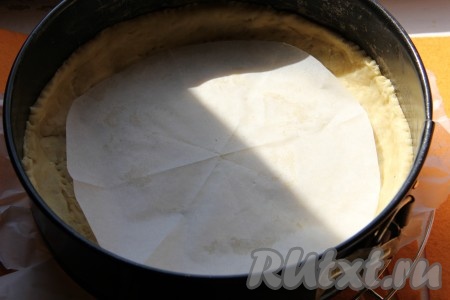 Форму для выпечки (у меня форма диаметром 28 сантиметров) смазать маслом. По истечении 30 минут достать тесто из холодильника, раскатать в пласт и выложить на дно формы для выпечки, формируя не очень высокий бортик. Сверху на тесто выложить пергаментную бумагу и на неё высыпать горох (или гречку), чтобы корж в духовке сильно не поднимался.