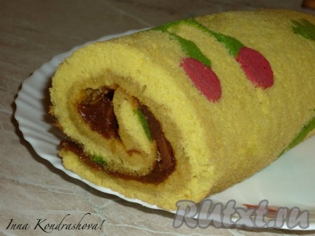Свернуть бисквит с начинкой в рулет, начиная с широкой стороны, помогая себе бумагой, на которой выпекался бисквит. На внешней стороны бисквитного рулета будет рисунок, который мы нанесли. Дать бисквитному рулету остыть и пропитаться начинкой. И можно подавать на стол.