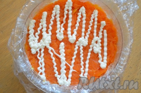 Следующим слоем разложить морковь, натёртую на крупной тёрке, утрамбовать, смазать майонезом.