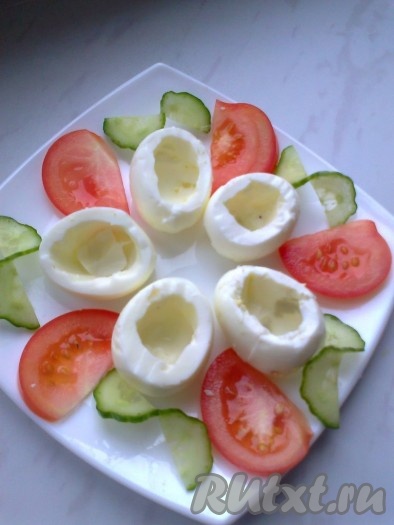 Углубить отверстие, чтобы было удобно накладывать салат. Половину помидора нарезать дольками и выложить на тарелку. От огурца отрезать 5 кружочков, разрезать почти до конца и развернуть половинки в противоположные стороны. Выложить на блюдо.