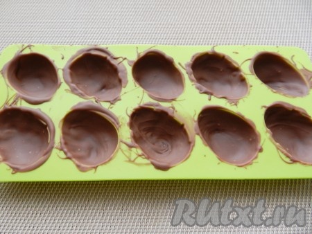 Расплавленный шоколад распределить по формочкам с помощью силиконовой кисти одним слоем и убрать в холодильник на 15-20 минут. Затем достать и нанести еще один слой шоколада. Проследить, чтобы не было просветов. После нанесения второго слоя формочки снова убрать в холодильник для застывания.