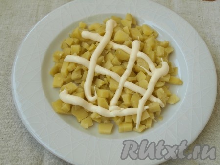 Картофель нарезать кубиками и выложить на плоское блюдо первым слоем. Сделать сеточку из майонеза.