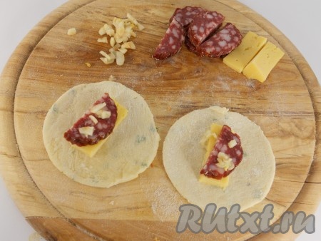 В центр каждого кружочка разместить начинку. В моем варианте - это ломтик сыра, кусочек колбасы и немного измельченного чеснока.