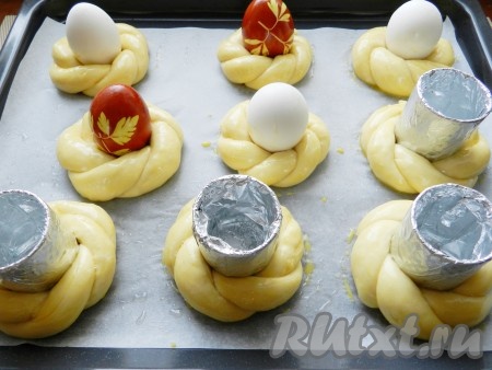 Соединить по два жгутика и скрутить их спиралью. Концы спирали соединить, чтобы получилось кольцо. Уложить булочки на противень, застеленный бумагой для выпечки и смазанный маслом.  В середину выложить вареные яйца. Так как такие булочки с вареными яйцами я пекла впервые, я решила подстраховаться и кроме вареных яиц воспользовалась обычными стеклянными стопками, обернув их фольгой и смазав маслом. Надо сказать, что второй вариант получился более удачным.