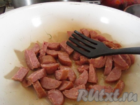 Колбасу нарежьте крупными кусочками и слегка поджарьте в глубокой сковороде на растительном масле.
