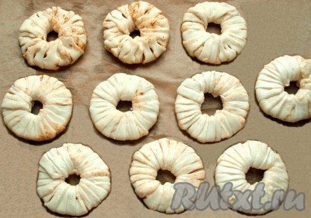 Полученными полосками слоеного теста обмотать кольца ананасов. На одно кольцо уйдёт приблизительно по две длинных полоски теста. Застелить противень пергаментом и выложить кольца на небольшом расстоянии друг от друга.
