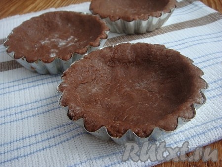 Тесто завернуть в пищевую пленку и отправить в холодильник примерно на 1 час.

Охлажденное тесто разделить на 12 равных частей. На доске, слегка присыпанной мукой (2 столовые ложки), из каждой части теста сформировать шарик. Каждый шарик выложить в формочки, формируя бортики.