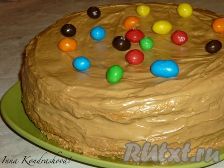 Выложить коржи друг на друга, смазывая их щедро кремом. Вареное сгущенное молоко взбить миксером с оставшимся сливочным маслом и смазать бисквитный торт сверху. Украсить конфетами&nbsp;m&m's.
