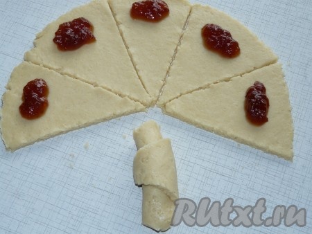 На основание каждого сегмента, отступив от края, выкладывать примерно по 0,5-1 чайной ложке густого джема. Сформировать творожный рогалик с начинкой, сворачивая каждый сегмент, начиная с широкой стороны.