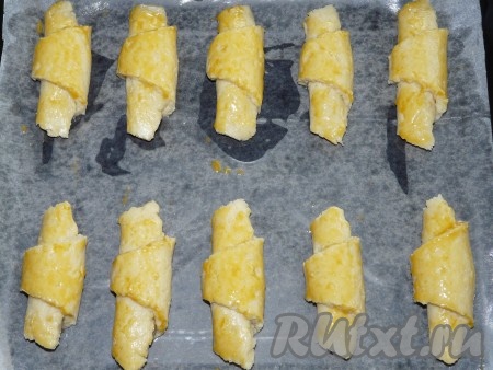 Скрученные творожные рогалики с джемом выложить на противень, застеленный пергаментной бумагой, и смазать взбитым желтком.