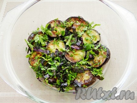 Затем вынуть и разложить слоем на дно стеклянной или эмалированной посуды. На каждый кусочек баклажана выложить чеснок и обильно присыпать зеленью.
